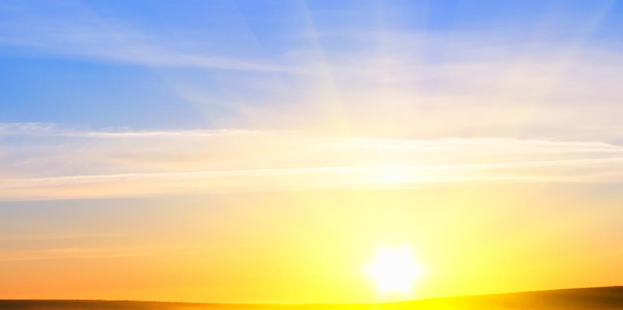Sol nascendo no horizonte sobre o mar e montanhas, como céu amarelado e azulado
