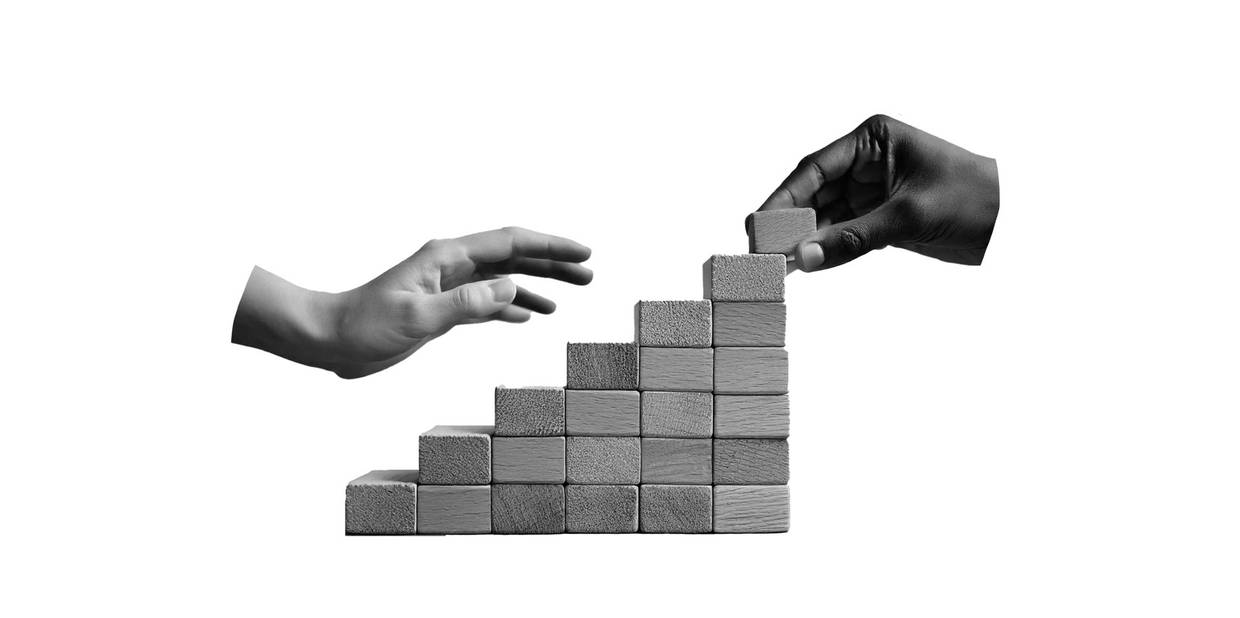 Duas mãos constroem, juntas, uma escada com blocos de madeira