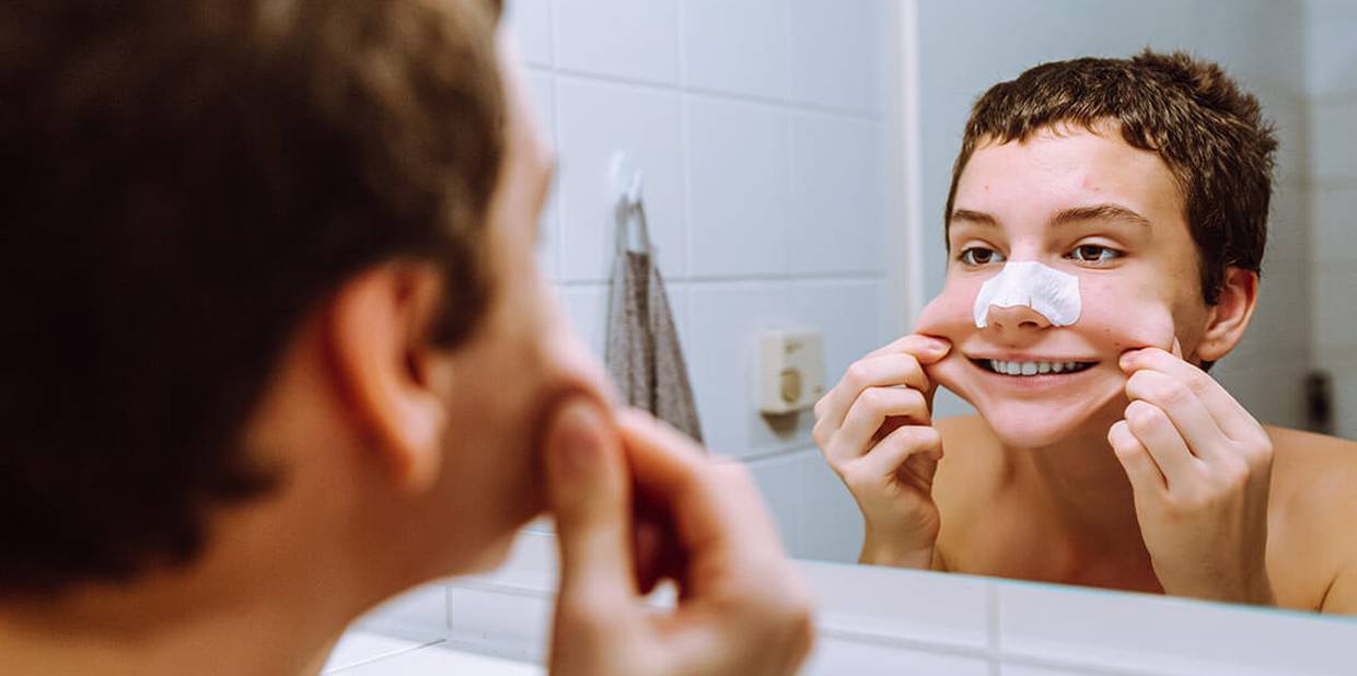 Adolescente se olha no espelho com adesivo para tirar cravos do nariz