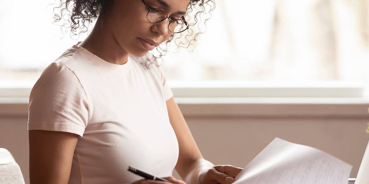 Mulher trabalha em uma mesa analisando e preenchendo papéis