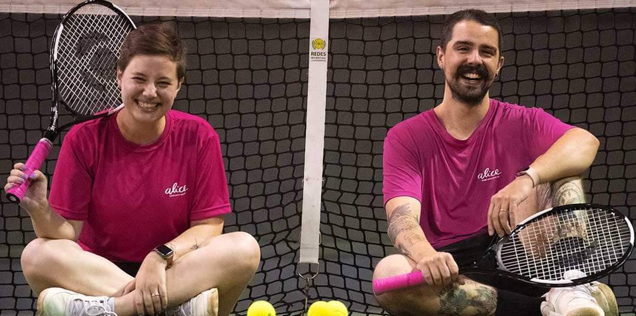 Mirella e Pedro sentados em uma quadra de tênis, segurando raquetes