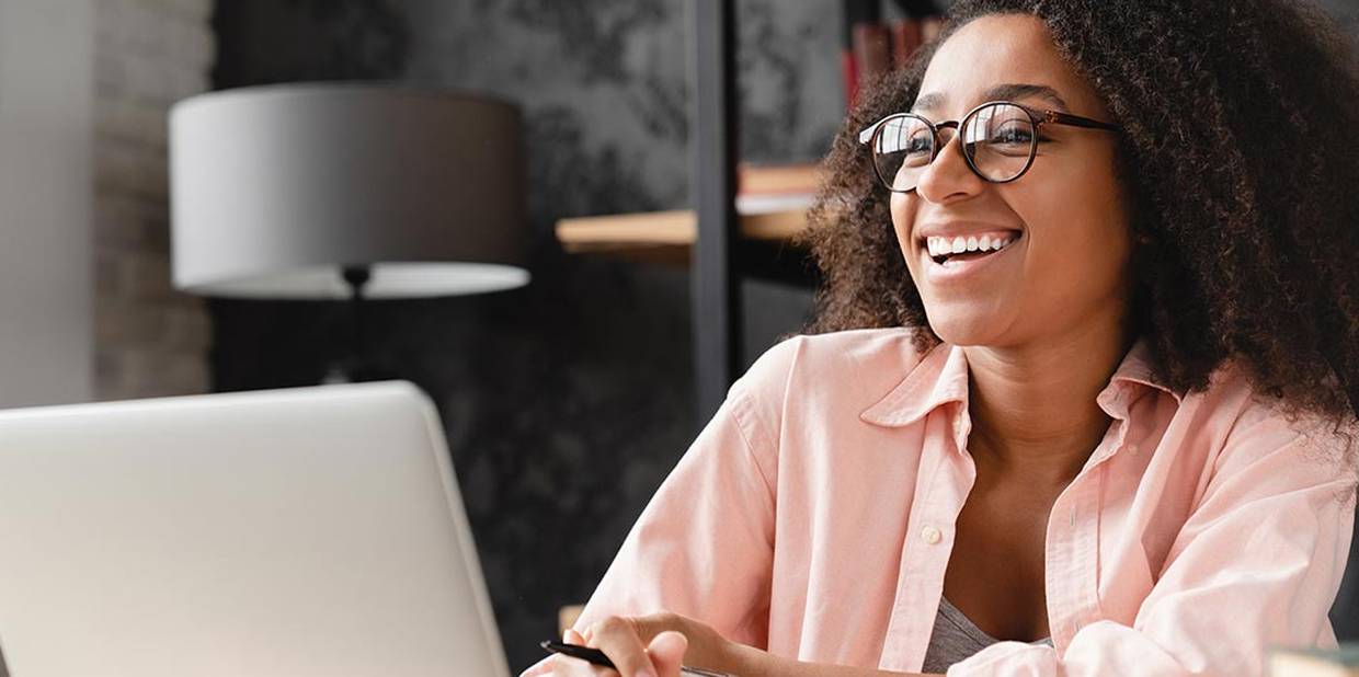 Mulher em escritório vestindo camisa rosa sorrindo para uma tela de computador