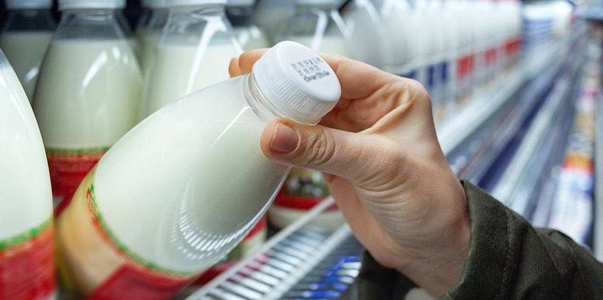 Close de mãos retirando uma garrafa de leite da prateleira