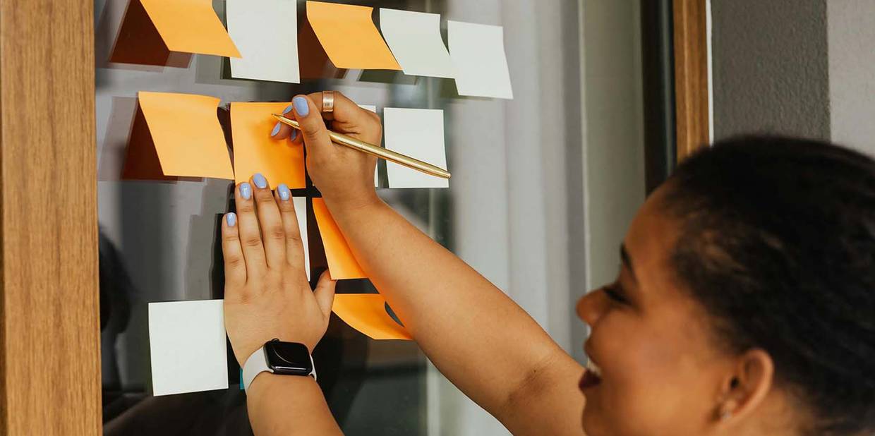 Uma mulher escreve em post it pendurados em uma parede