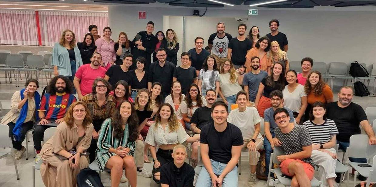 Diversas pessoas que trabalham na Alice posam sorrindo para uma foto. Alguns estão sentados e outras pessoas estão de pé.