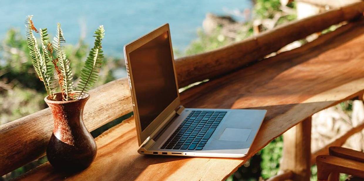 Computador em cima de mesa com mar ao fundo