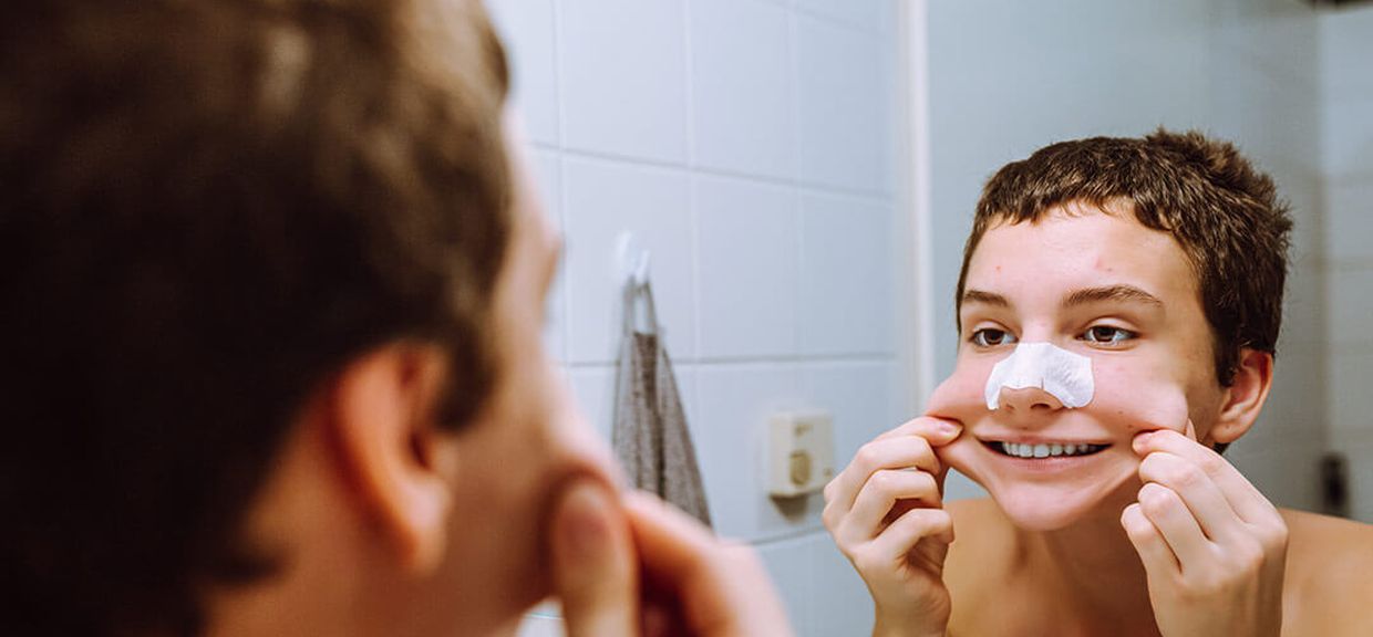 Adolescente se olha no espelho com adesivo para tirar cravos do nariz