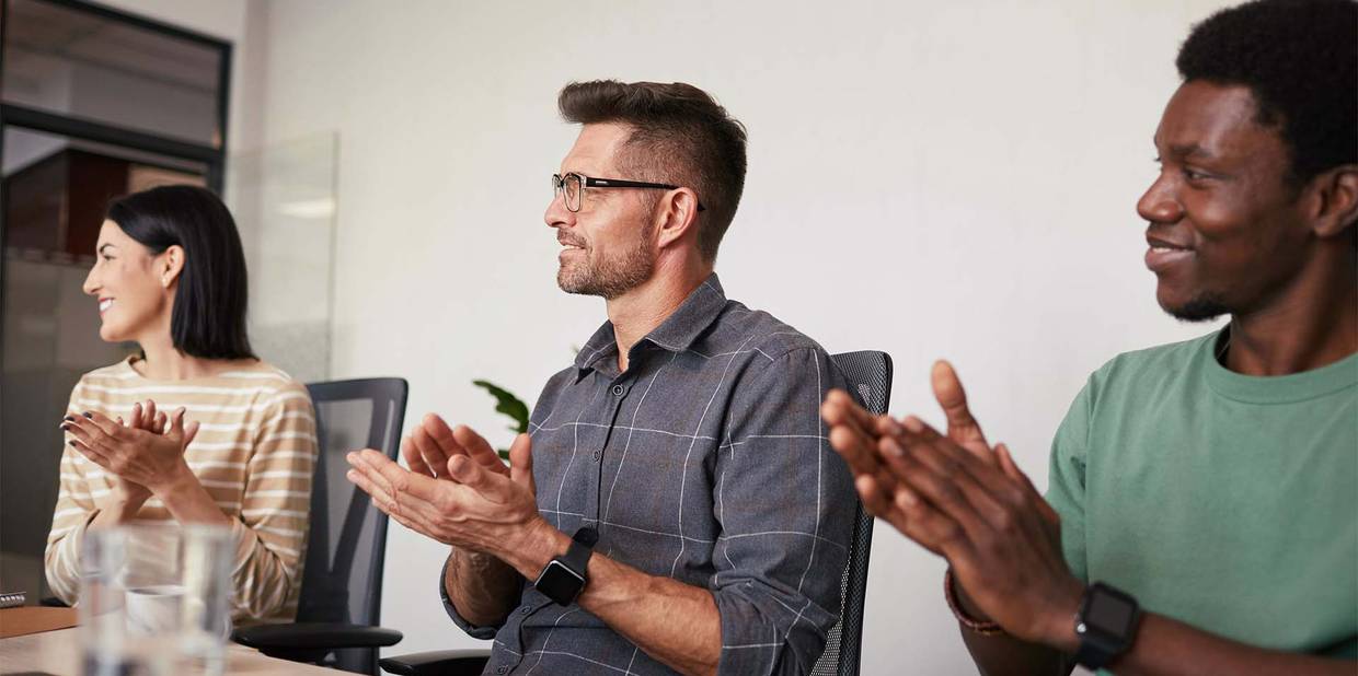 Dois homens e uma mulher estão em uma mesa de reunião