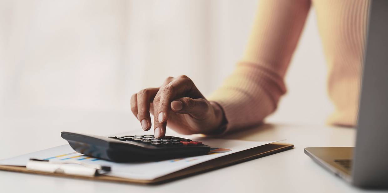 O braço de uma pessoa está está mexendo em uma calculadora em cima de uma mesa branca