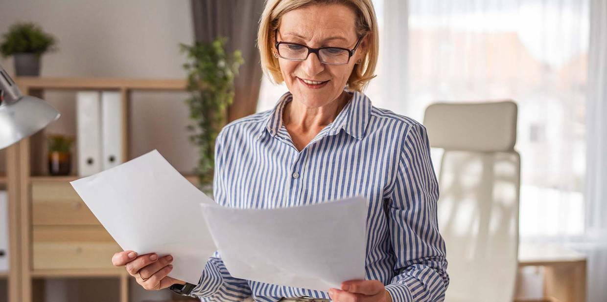 Uma mulher usando óculos segura e analisa papeis em sua mão