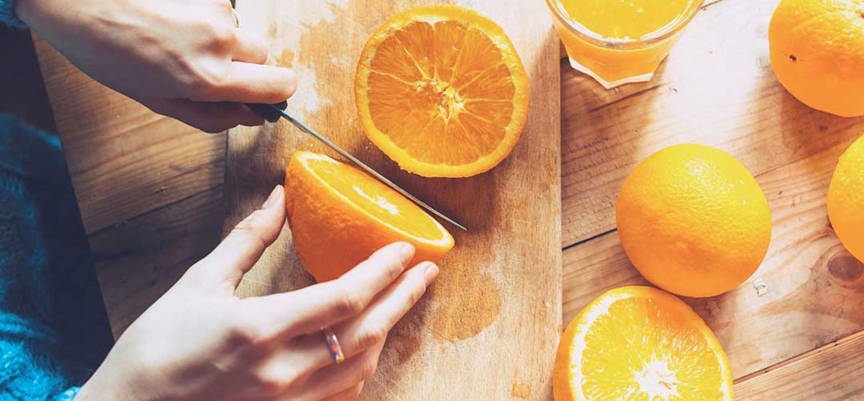 Close das mãos de uma mulher cortando laranjas, um dos alimentos que podem piorar a afta