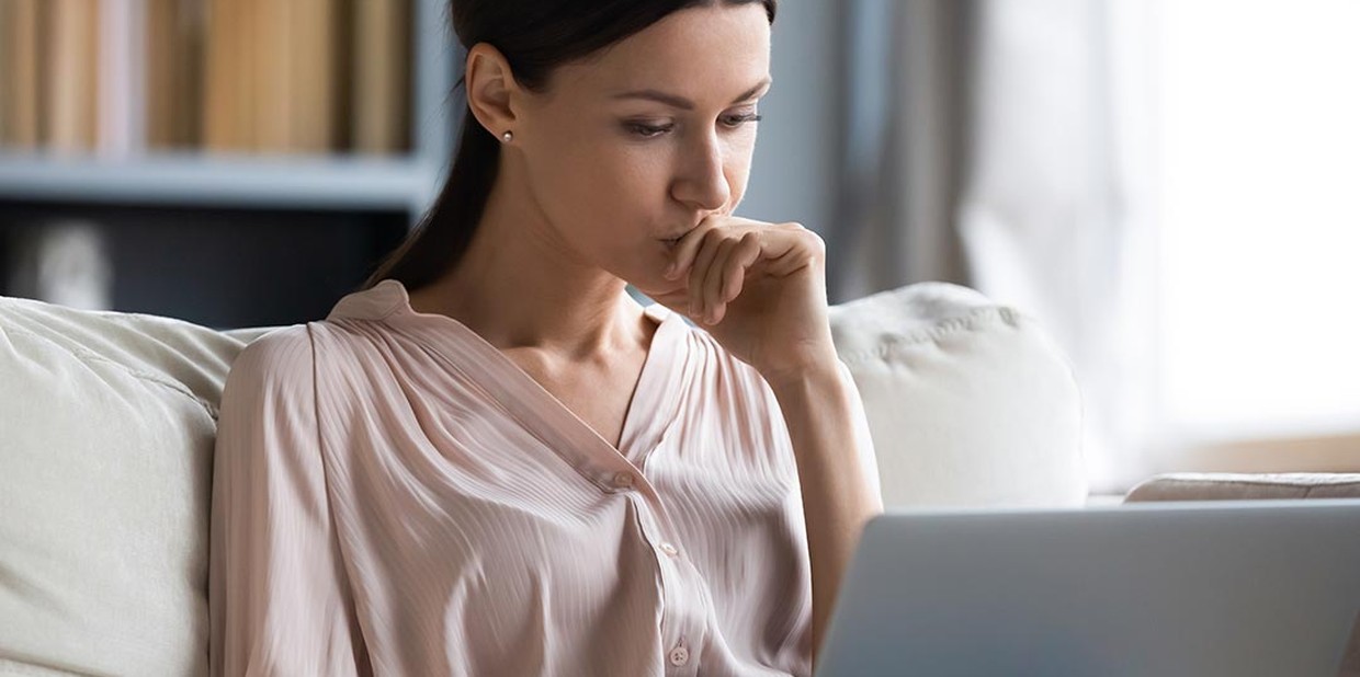 Mulher sentada no sofá com um notebook no colo e expressão de dúvida