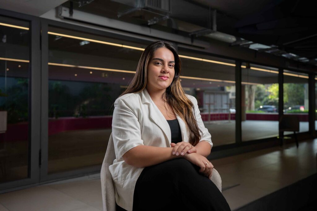 Uma mulher está sentada em uma cadeira, com as mãos na perna, olhando para frente